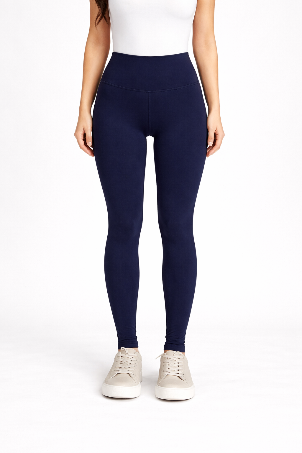 Person wearing navy leggings and white sneakers on a white background