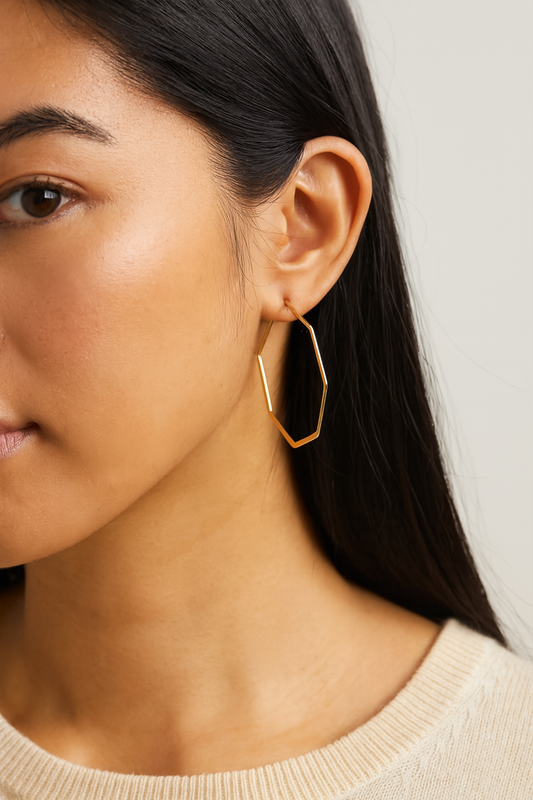 Close-up of a person wearing gold hoop earrings with a neutral background