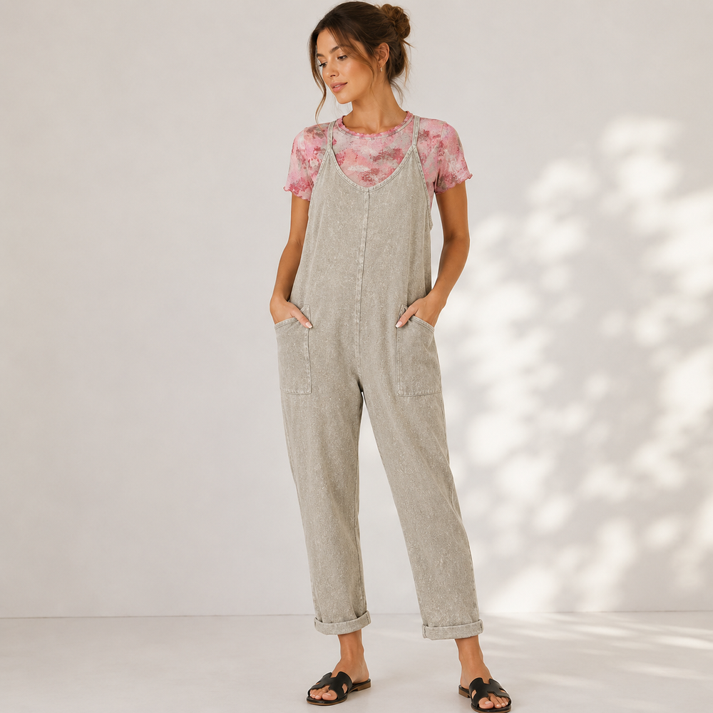 Woman wearing a light gray overalls and pink floral top against a white background