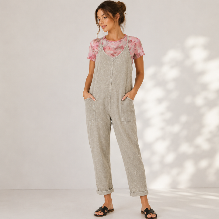 Woman wearing a light gray overalls and pink floral top against a white background