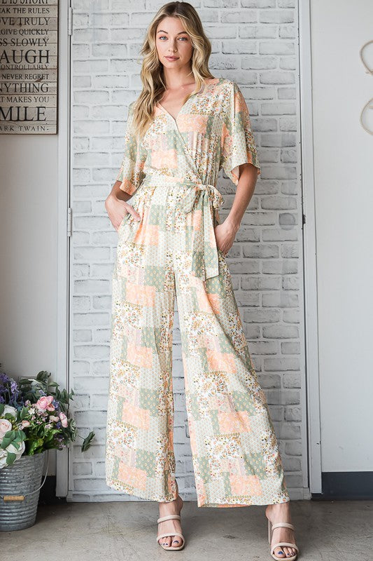 Woman wearing a floral jumpsuit standing against a white brick wall.