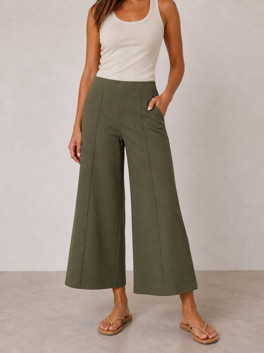 Person wearing a white tank top and green wide-leg pants on a plain background