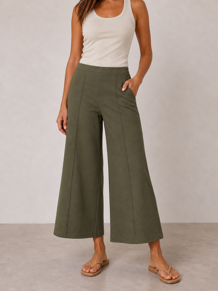 Person wearing a white tank top and green wide-leg pants on a plain background