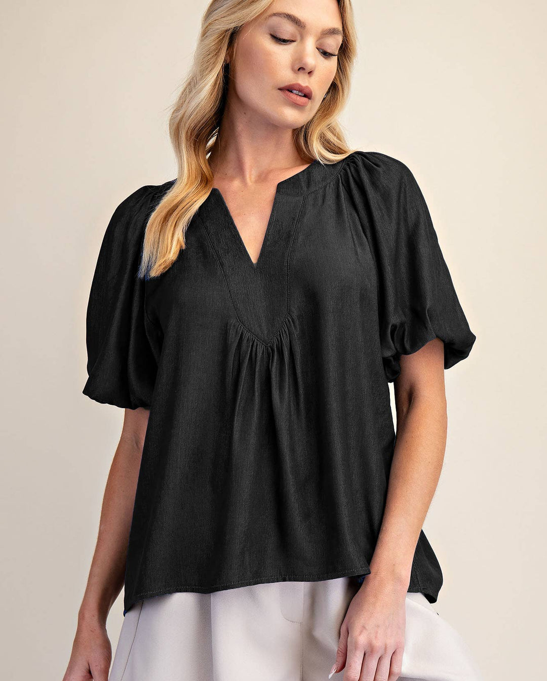 Woman wearing a black blouse and white shorts on a beige background