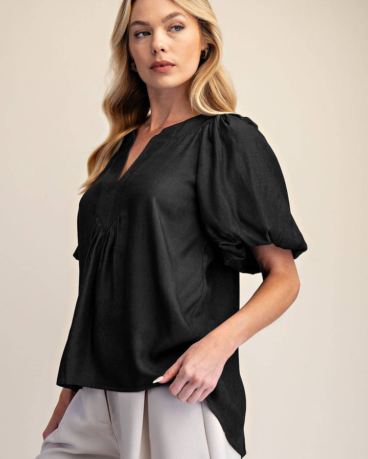 Woman wearing a black blouse with puff sleeves and light gray shorts on a beige background