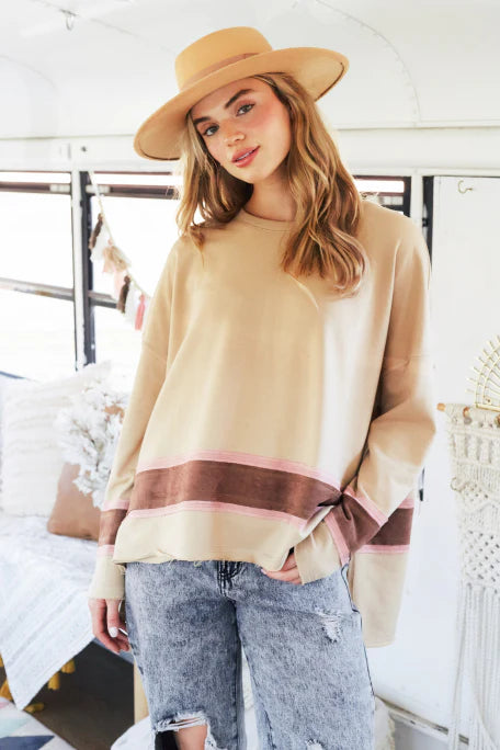 Woman wearing a beige sweater with a striped hem and a wide-brimmed hat indoors.