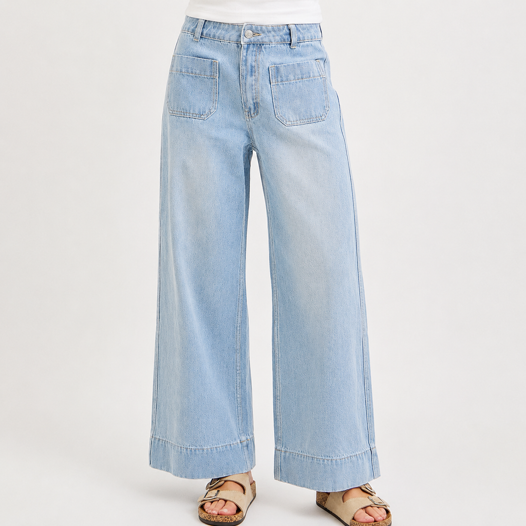 Light wash wide-leg denim jeans shown on a model from the waist down, paired with a white top and tan sandals against a plain light gray studio background.