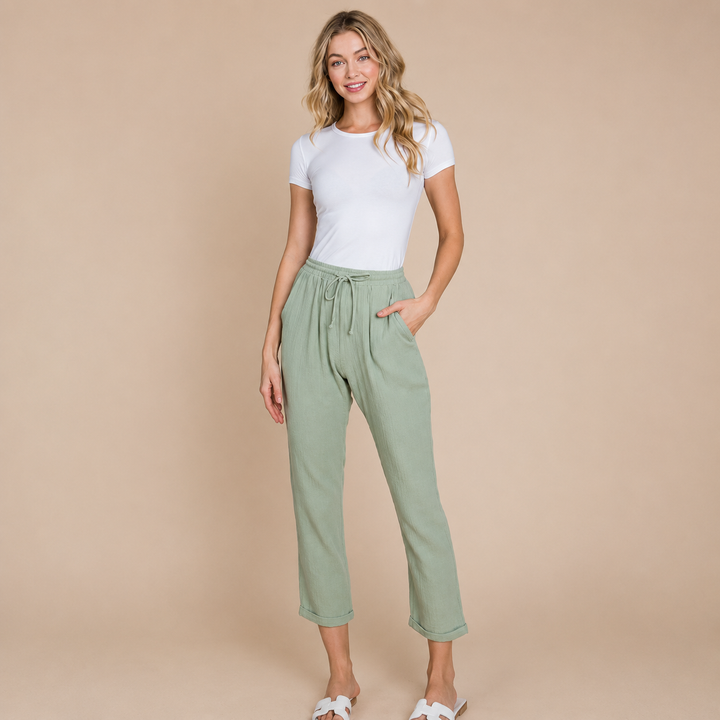 Woman wearing a white t-shirt and green pants against a beige background