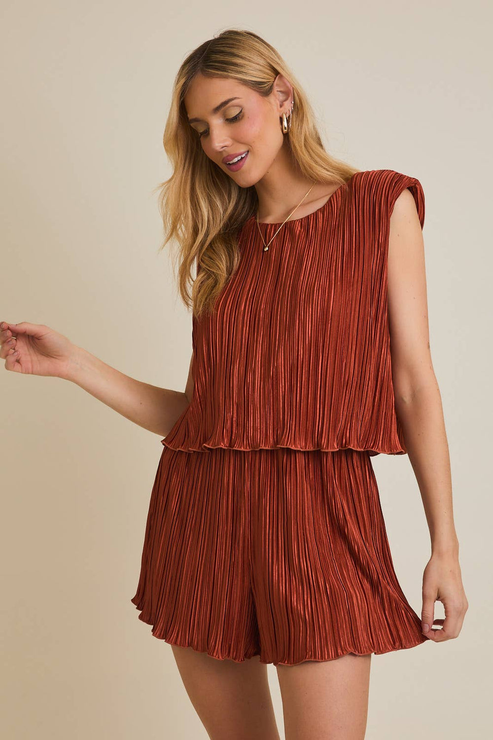 Woman wearing a rust-colored pleated top and shorts set against a beige background