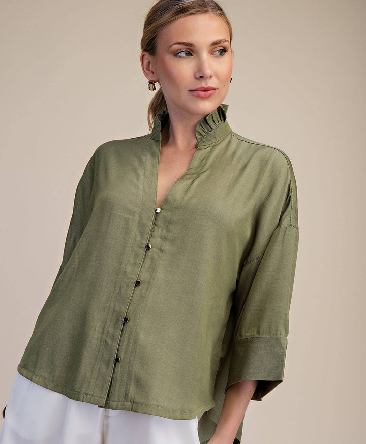 Woman wearing an olive green blouse and white shorts on a beige background