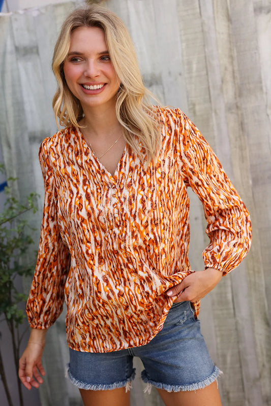 Woman wearing an orange and white patterned blouse with denim shorts against a wooden fence background