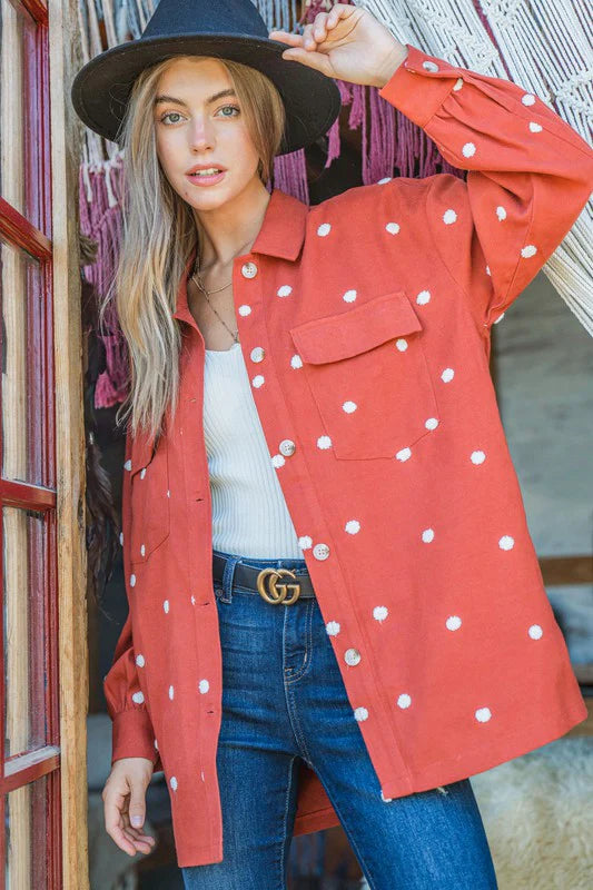 Woman wearing a red polka dot jacket, white top, and blue jeans with a black hat.
