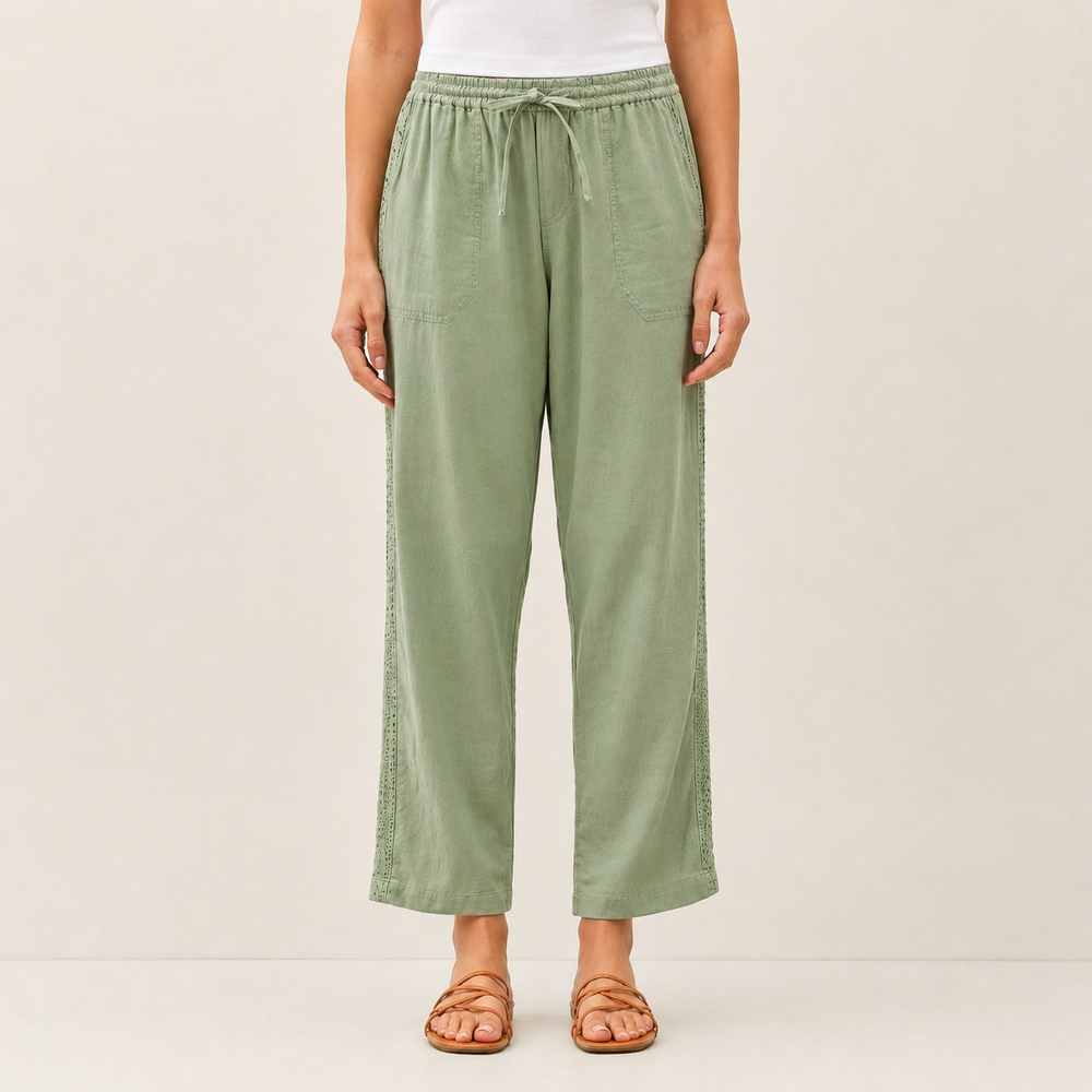 A model is wearing sage green wide-leg cropped pants with a drawstring waist, paired with a white top and brown strappy sandals, against a plain beige studio background.