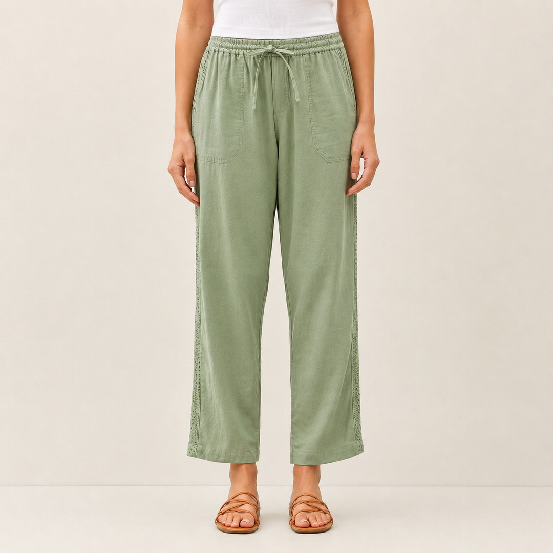 A model is wearing sage green wide-leg cropped pants with a drawstring waist, paired with a white top and brown strappy sandals, against a plain beige studio background.
