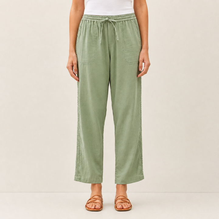A model is wearing sage green wide-leg cropped pants with a drawstring waist, paired with a white top and brown strappy sandals, against a plain beige studio background.