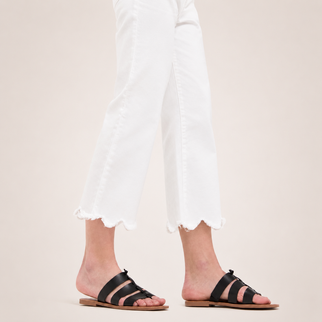Black sandals worn with white pants on a neutral background