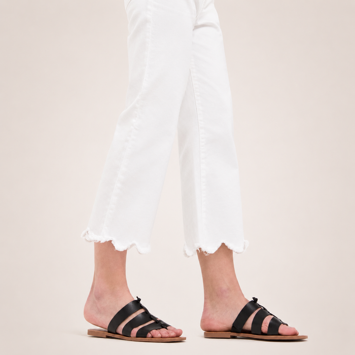 Black sandals worn with white pants on a neutral background