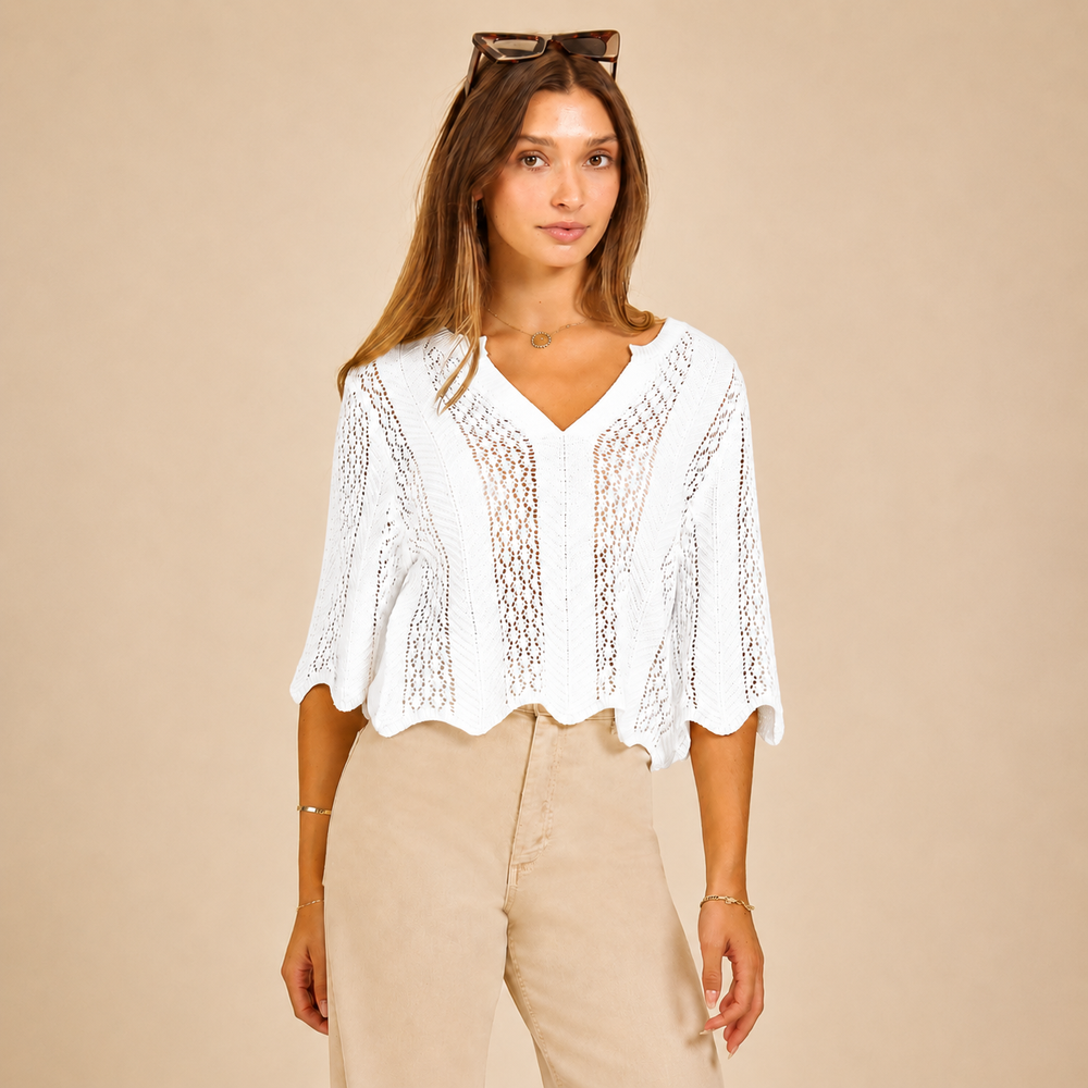 Woman wearing a white lace top and beige pants against a beige background