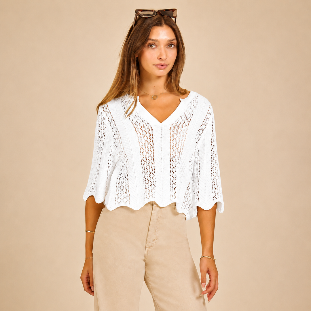 Woman wearing a white lace top and beige pants against a beige background