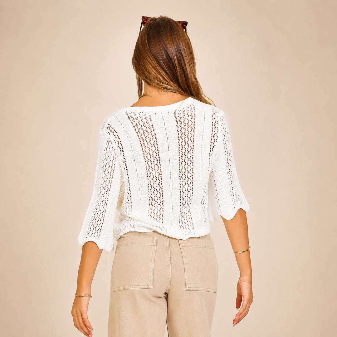 Woman wearing a white lace top and beige pants against a beige background