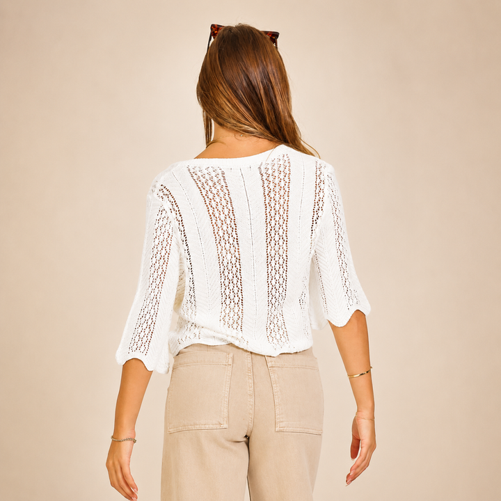 Woman wearing a white lace top and beige pants against a beige background