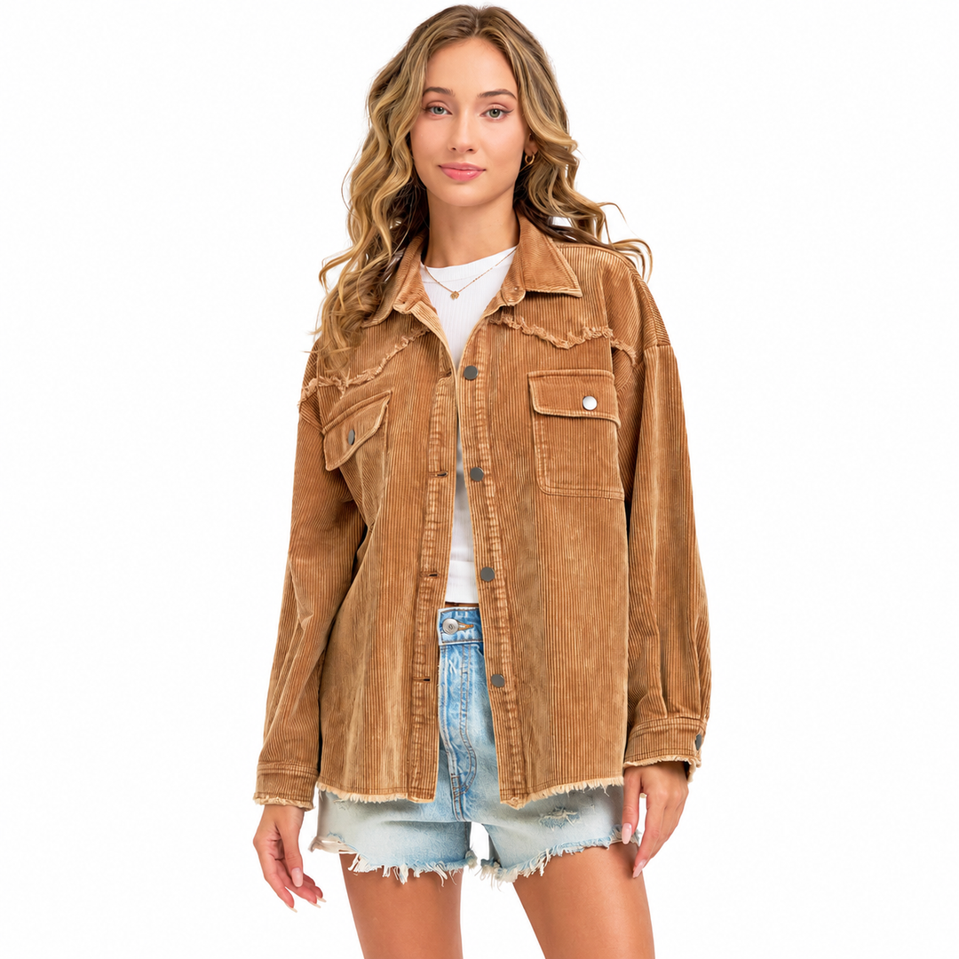 A woman modeling an oversized tan corduroy jacket with raw, frayed edges, worn over a white t-shirt and light-wash denim shorts against a solid white background.