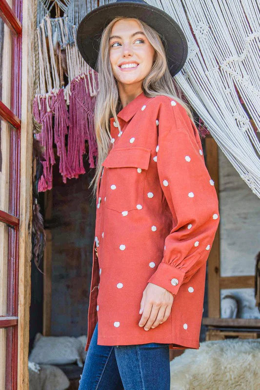 Woman wearing a red polka dot coat and hat, standing in a rustic setting.