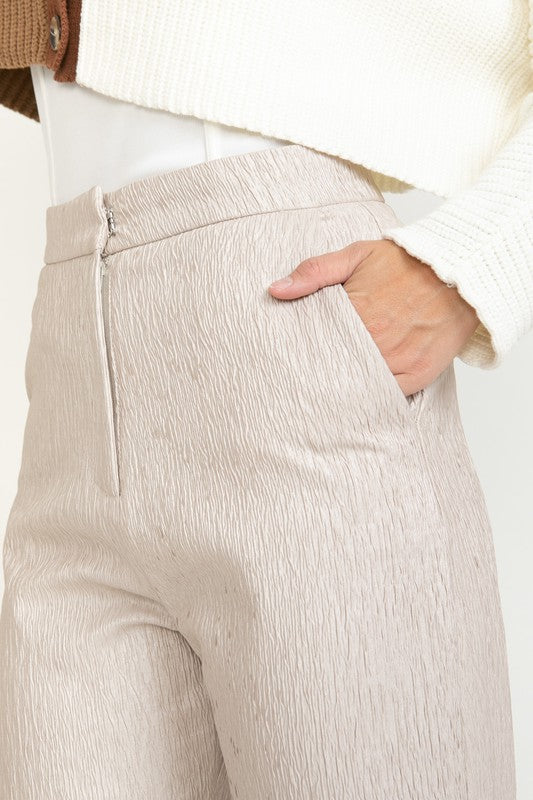 Close-up of beige pants with a white shirt underneath on a plain background