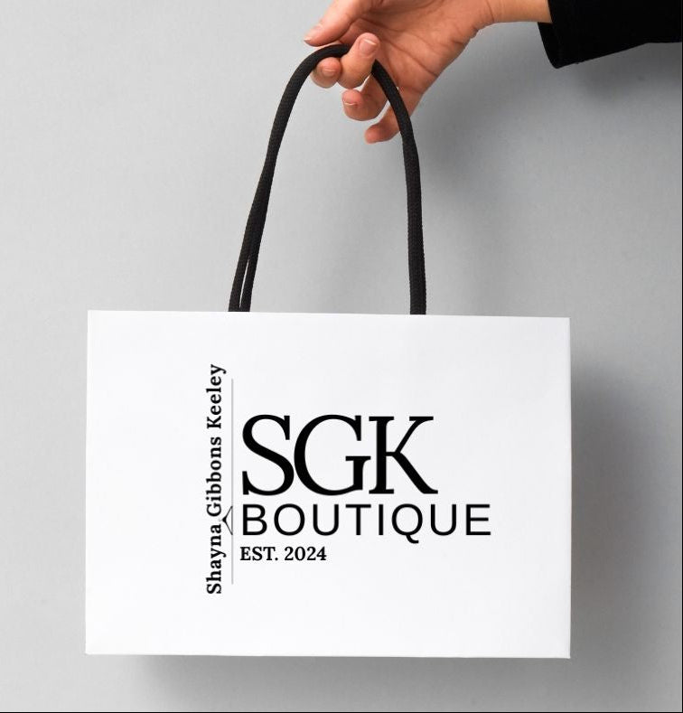 White shopping bag with 'SGK Boutique' branding held by a hand on a gray background
