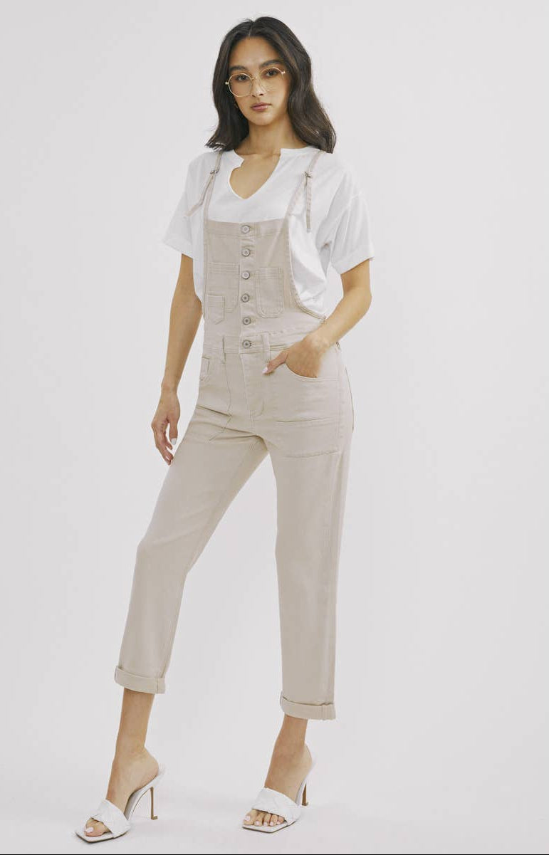 Woman wearing a beige overalls outfit on a white background