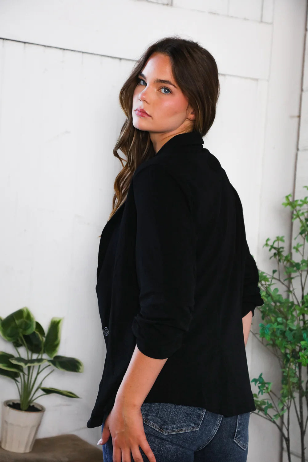 Woman wearing a black shirt and blue jeans standing indoors with plants in the background