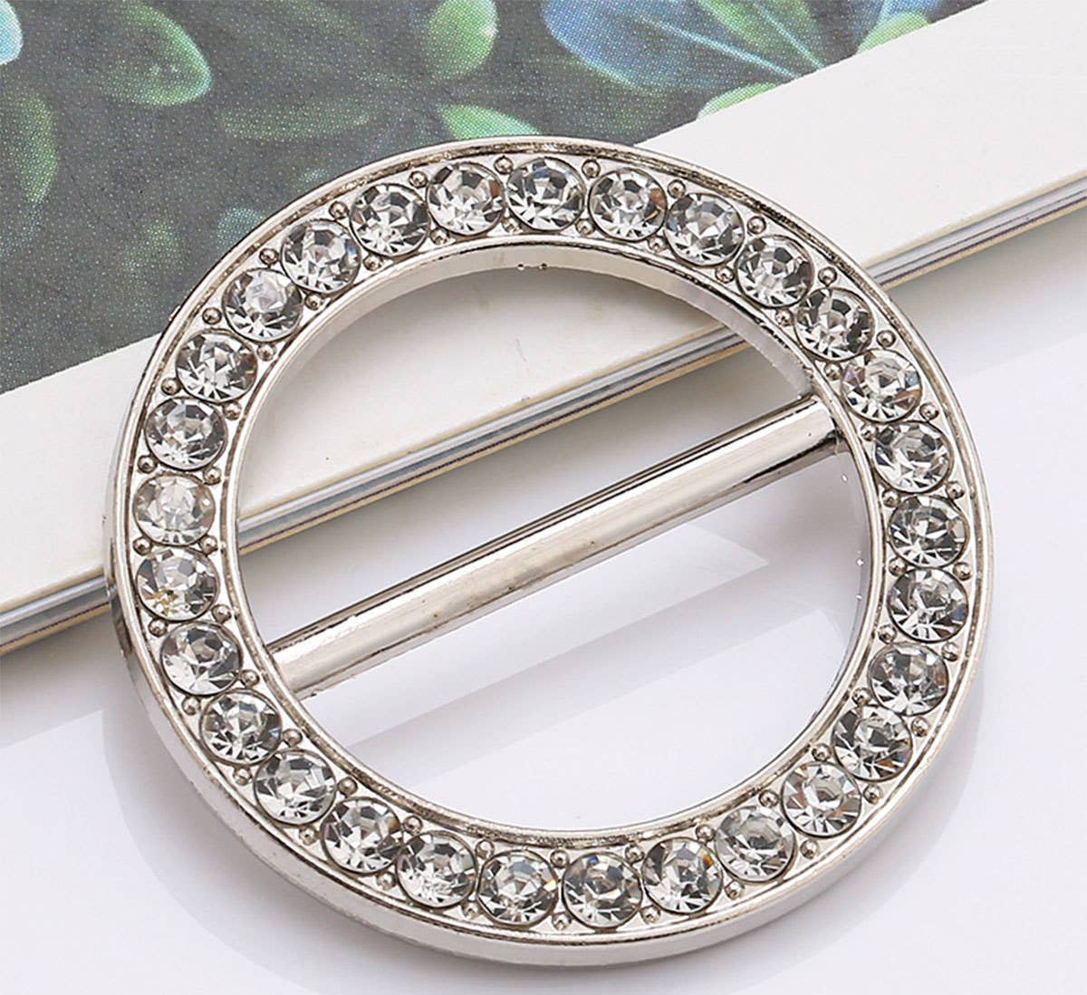 Circular metal brooch with crystal embellishments on a white surface