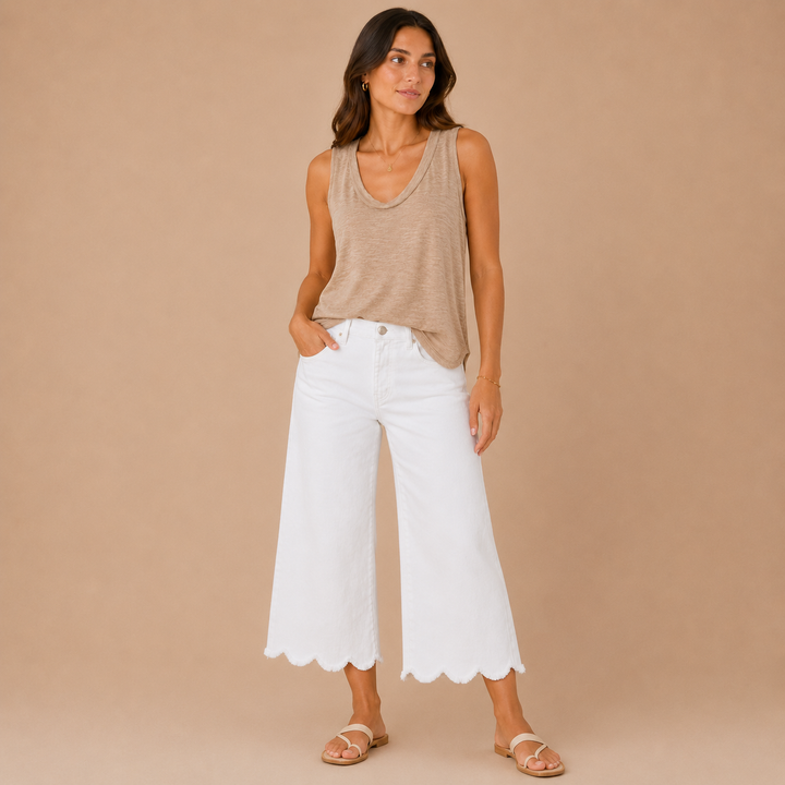 Woman wearing a beige sleeveless top and white pants on a beige background