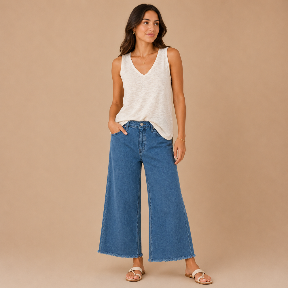 Woman wearing a white sleeveless top and blue jeans on a beige background