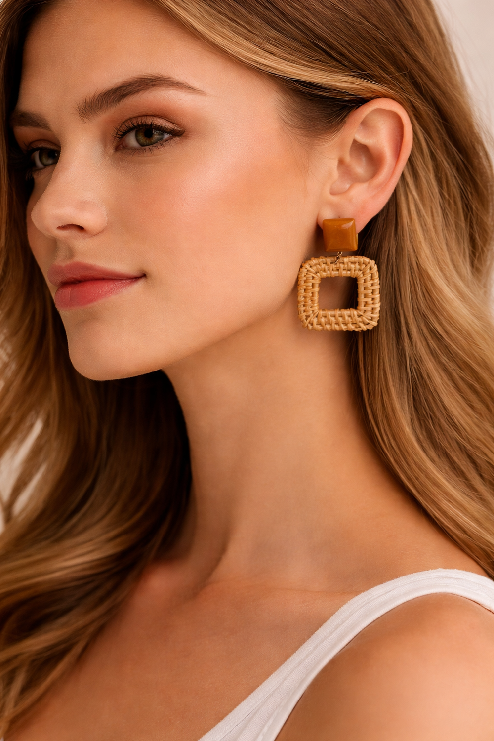 Close-up of a woman wearing gold square earrings with a neutral background