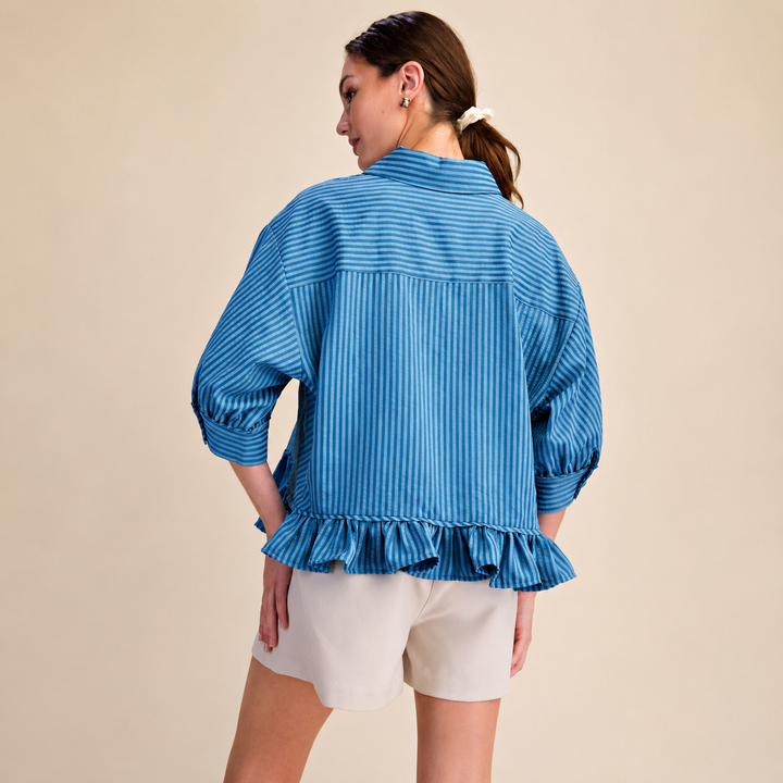 Woman wearing a blue striped blouse with ruffled details on a beige background
