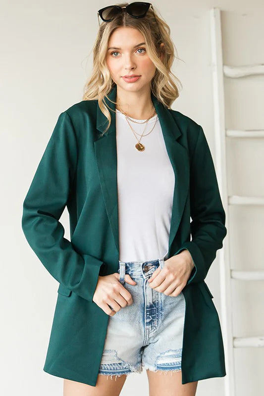 Woman wearing a green coat over a white shirt and denim shorts indoors.