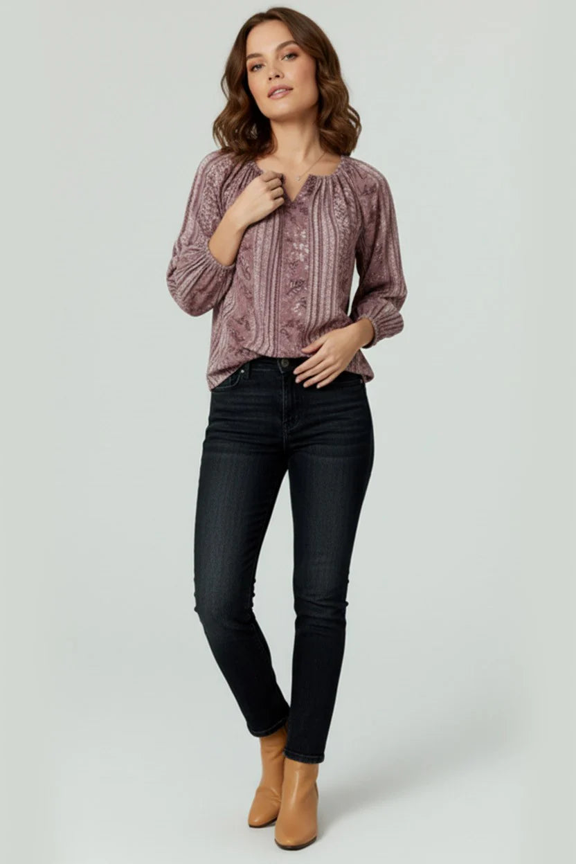 Woman wearing a patterned blouse, black jeans, and tan boots on a light gray background
