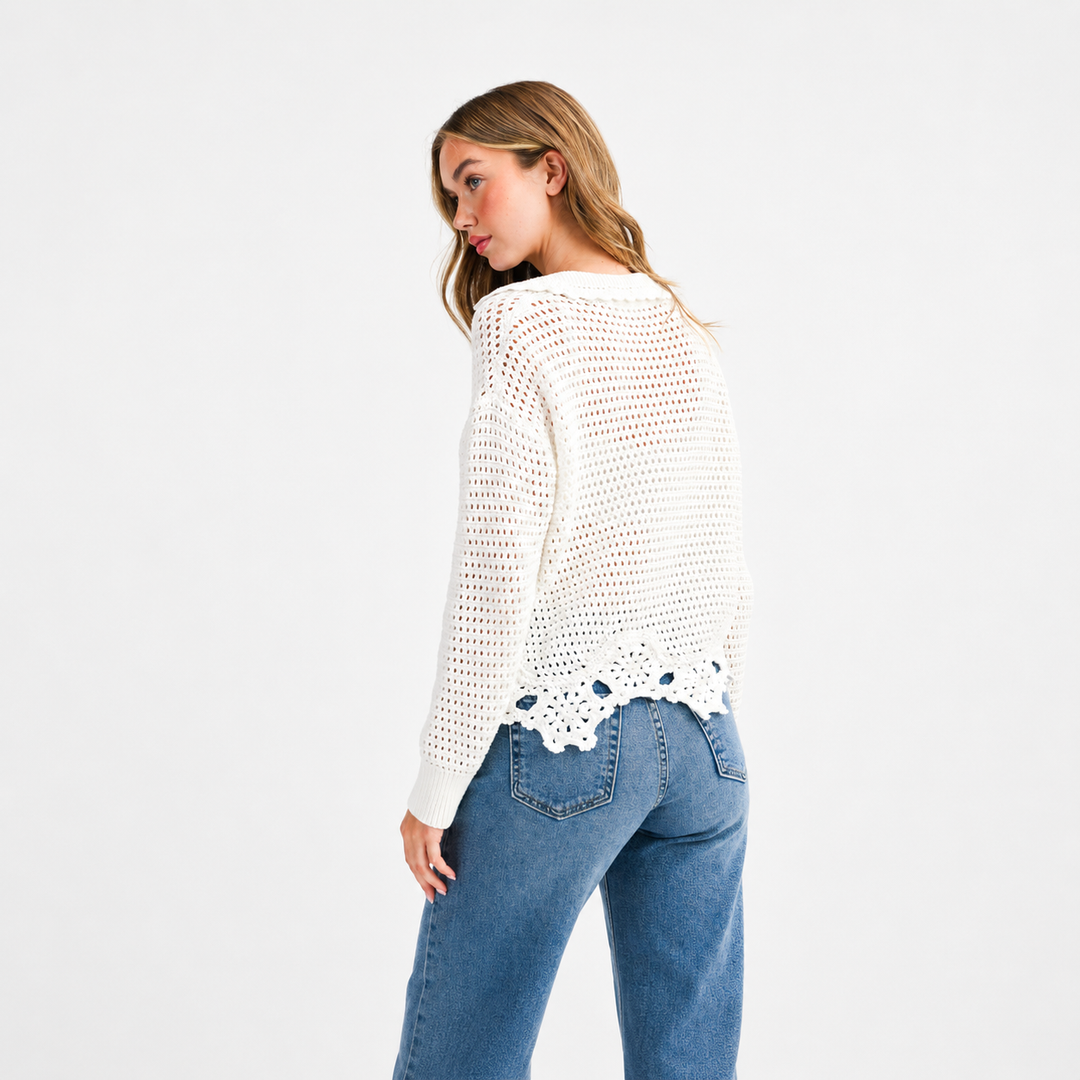 Woman wearing a white crochet sweater with lace details on a plain background