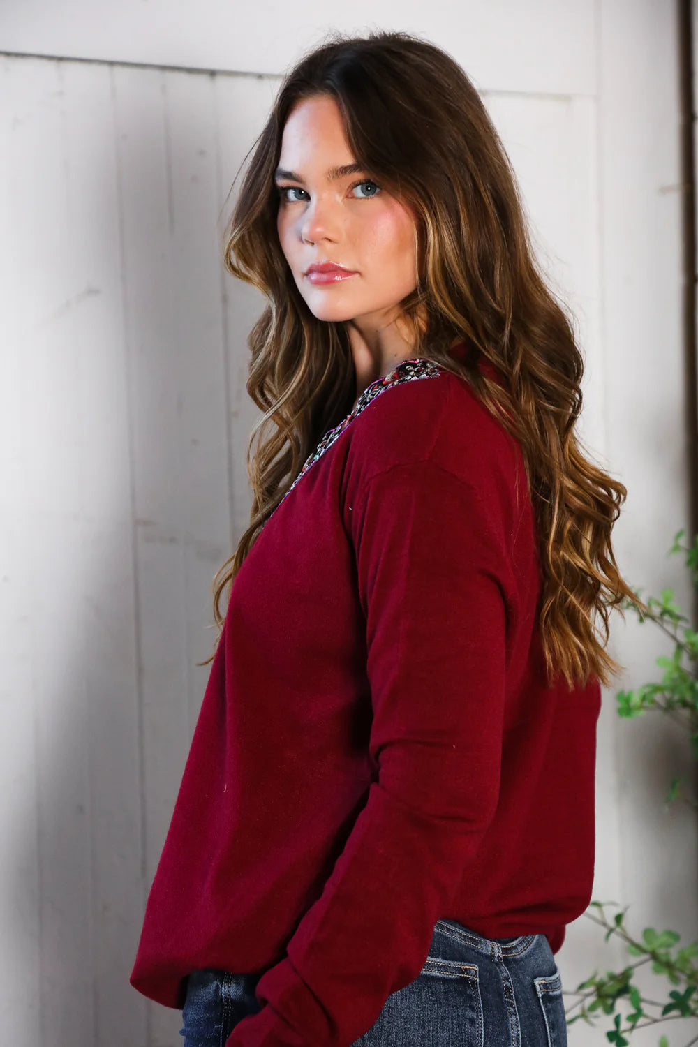 Woman wearing a Wine sweater and blue jeans against a white wooden background