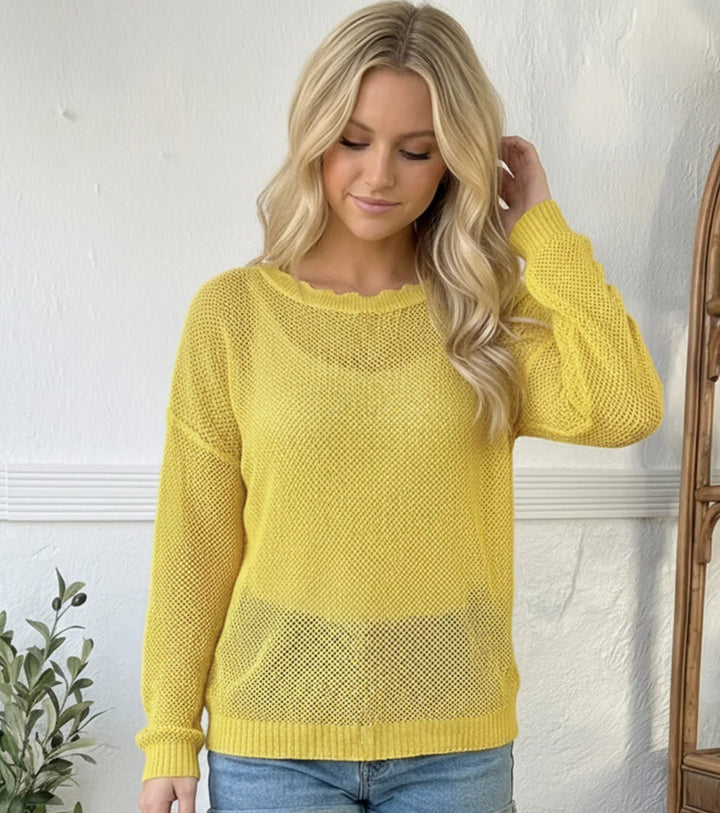 Woman wearing a yellow sweater and denim shorts against a white wall.